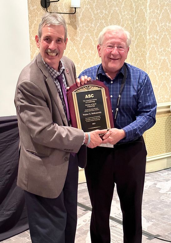 Dr. Dekeseredy smiling while holding his award with friend