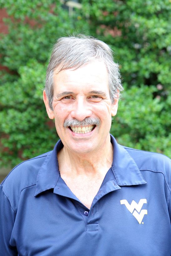 Dr Dekeserdy smiling. wearing a blue WV shirt. Trees behind him.  